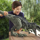 A child plays with a giant dinosaur toy as it hovers its open jaw over a tiny dinosaur toy.
